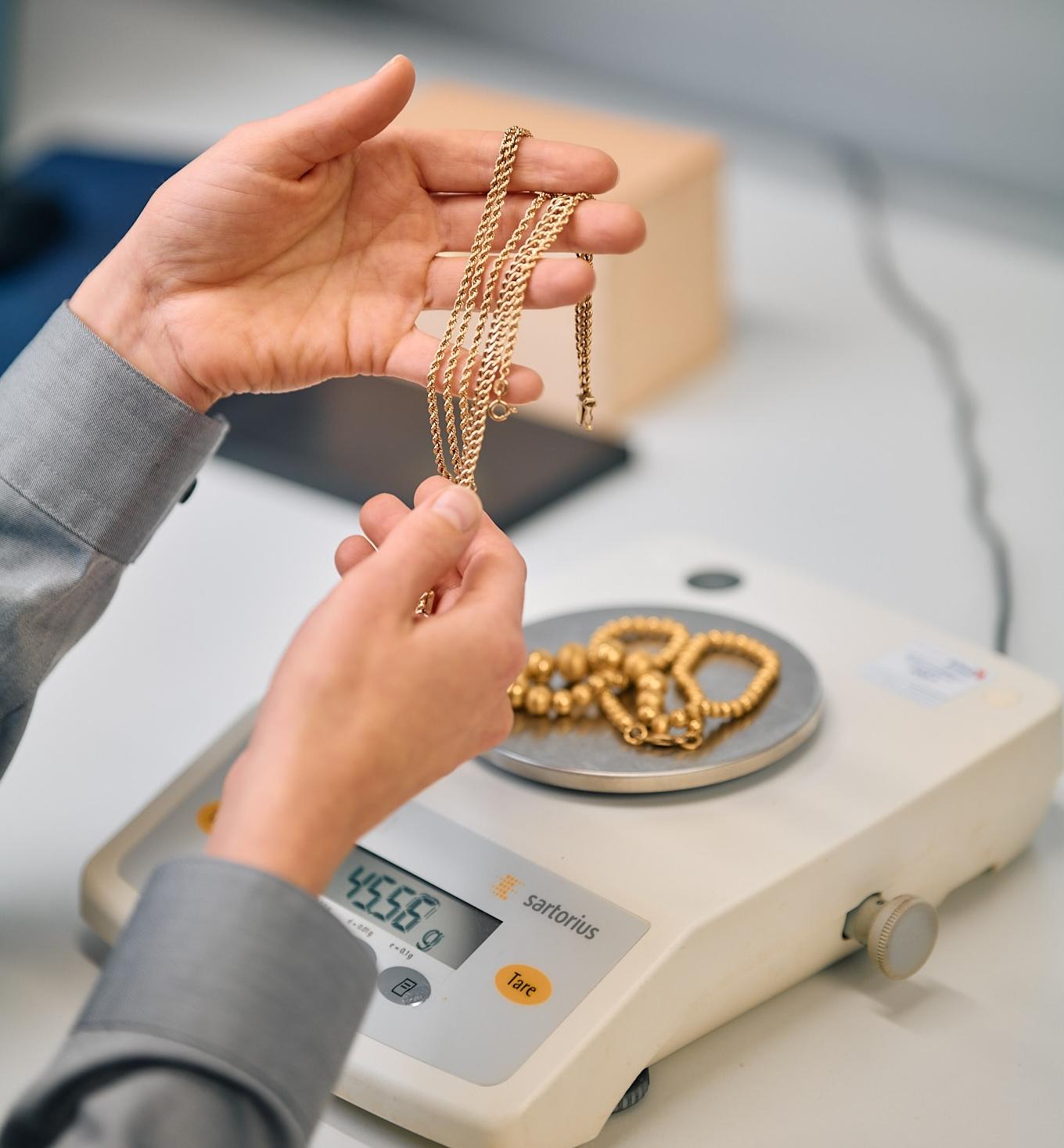 Kultaketju Jalonom asiantuntijan käsissä, taustalla satorius-merkkinen vaaka jonka päällä on paksu kultaketju.